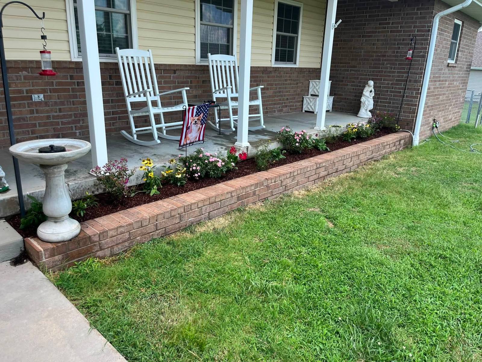 Brick-edged porch flower bed with coneflowers and roses