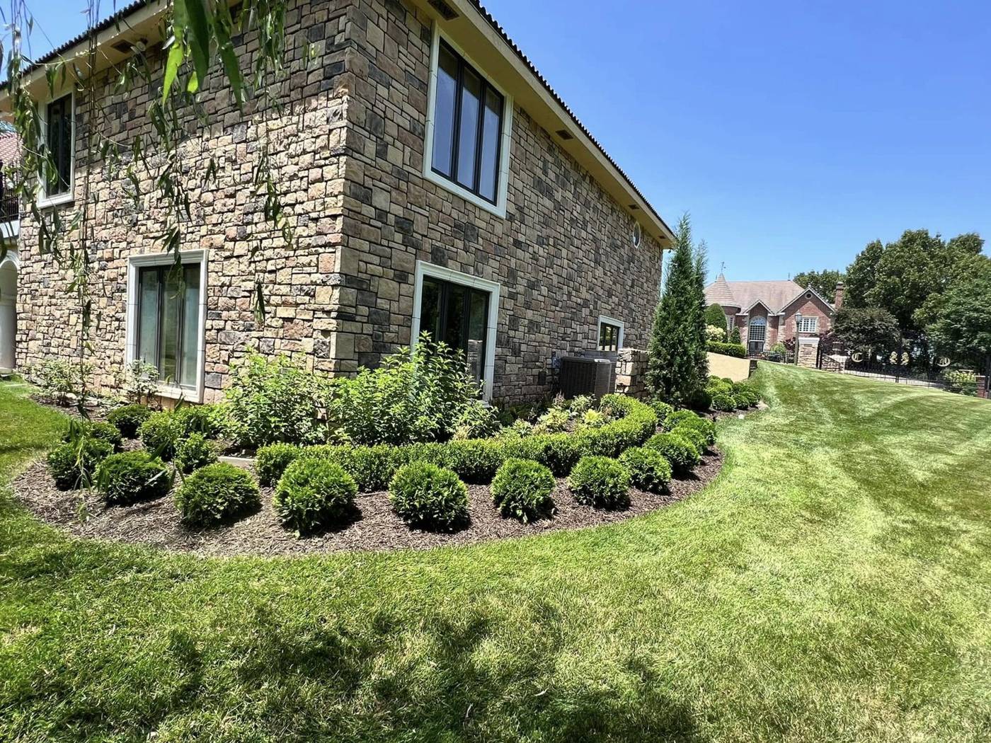 Striped lawn and trimmed boxwoods along a stone home